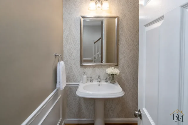 Powder room with a white pedestal sink, framed mirror and wall lights, a small room guests notice first.