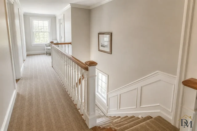Upstairs landing and staircase with white balusters, a wood handrail and a carpet runner, vacuumed step by step.